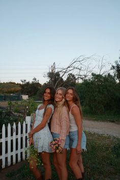 three girls standing next to each other in front of a white fence