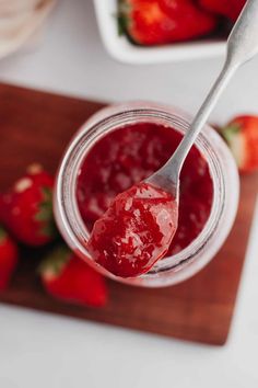 a spoon full of strawberry jam sitting on top of a cutting board