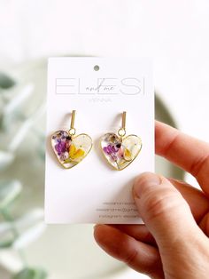 a pair of earrings with flowers in the shape of a heart on a white card