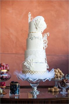 a three tiered wedding cake sitting on top of a glass table next to grapes and nuts