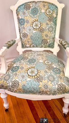 a white chair with blue and yellow flowers on it's armrests sitting on a wooden floor