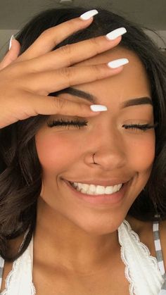 a woman smiling and holding her hands to her forehead with white nail polish on it