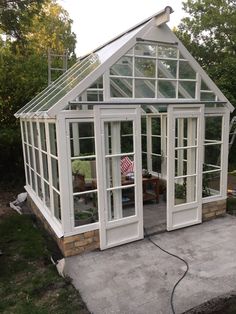 a small white greenhouse with glass doors and windows on the side of it's roof