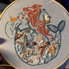 someone is holding up a hand embroidered hoop with an image of a mermaid and seashells on it