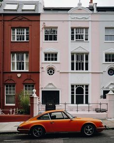 an orange car is parked in front of some colorful buildings on a city street,