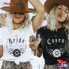 two women wearing hats and t - shirts holding wine glasses in front of their faces