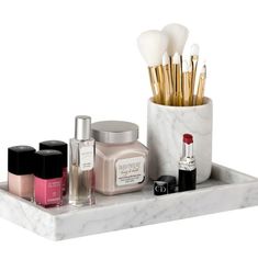 a marble tray with makeup brushes, lipstick and nail polishes on it in front of a white background