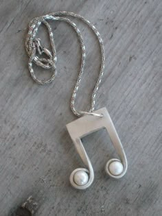 a musical note necklace on a wooden surface with a silver chain and two white beads