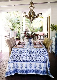 a dining room table with blue and white cloths on it, next to a chandelier