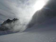 the sun shines through clouds on top of a snowy mountain