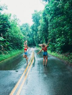 two women in bathing suits are dancing on the road with trees and bushes behind them