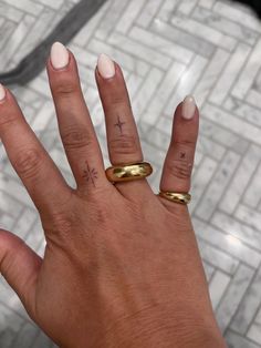 a woman's hand with two gold rings on her fingers and one has a cross tattoo on it