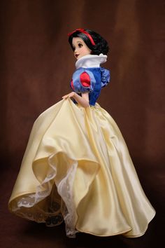 the snow queen doll is wearing a white dress and red headband, while standing in front of a brown background