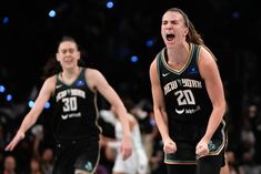 two female basketball players in black uniforms are on the court and one has her mouth open