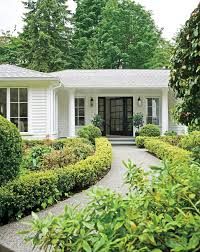 a white house surrounded by trees and bushes with a black door in the front yard