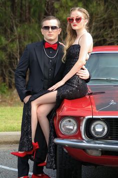 a man and woman sitting on the hood of a red car