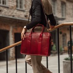 a woman carrying a red leather briefcase on her shoulder while walking down the stairs in front of a building