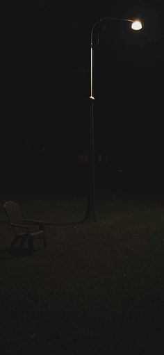 a park bench sitting under a street light in the dark with a lamp post behind it