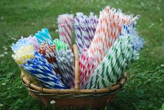 a basket filled with lots of different colored paper straws on top of a green grass covered field