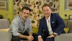 two men sitting on couches in a living room with yellow walls and patterned curtains