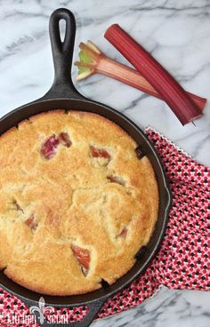 a cast iron skillet with a pie in it and rhubarb stalks next to it