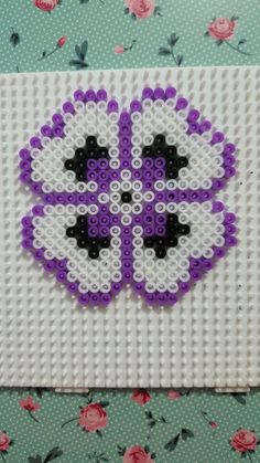 a purple and white beaded flower on top of a green background with pink roses