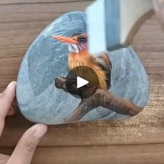 a bird sitting on top of a wooden table next to a person's hand