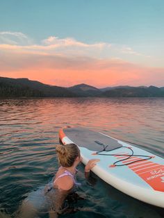 a woman standing in the water with a surfboard on her back while she looks at the sunset