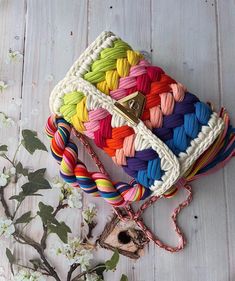 multicolored crochet purse on white wooden table next to flowers and branches