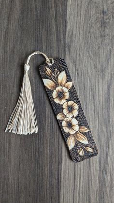 a bookmark with flowers on it sitting on a wooden table next to a tassel