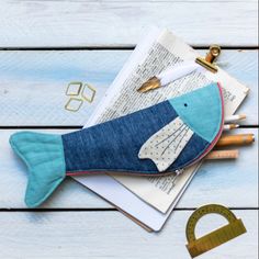 a fish shaped purse sitting on top of an open book next to rulers and pencils