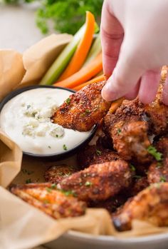 a person dipping sauce on top of chicken wings with carrots and celery