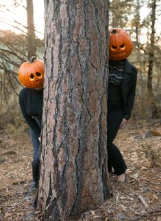 two people with pumpkin heads hiding behind a tree