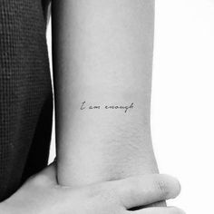 a woman's arm with a small tattoo saying i am enough on the wrist