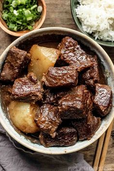 beef and potatoes in a bowl with chopsticks next to it on a wooden table