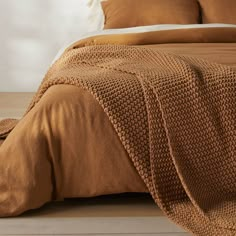 a bed covered in brown linens and pillows on top of a wooden floor next to a white wall