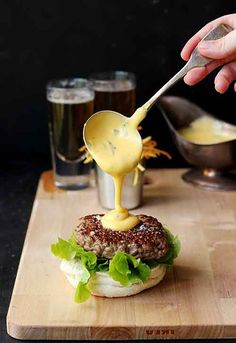 a person pouring mustard onto a burger on a cutting board