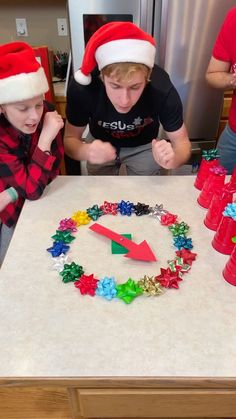 two boys in santa hats are making christmas decorations on a table with red plastic cups