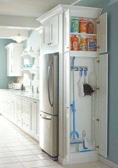 a kitchen with blue walls and white cabinets has cleaning supplies in the bottom cabinet, including brooms and mop's