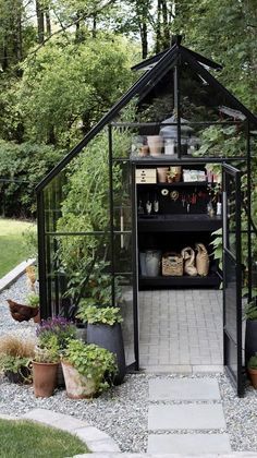 a small greenhouse with lots of potted plants and pots on the ground in front of it