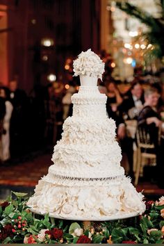 a large white wedding cake sitting on top of a table in front of other people