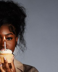 a woman holding a cupcake with a lit candle in her mouth