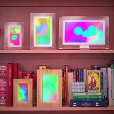 some books are sitting on a shelf in front of two framed pictures, one is pink and the other is green