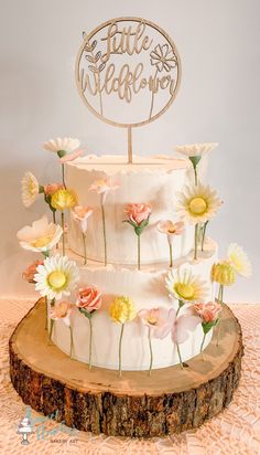 a three tiered cake with flowers on the side and a wooden sign that says, little wildflowers