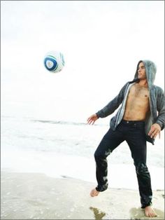 a shirtless man playing with a soccer ball on the beach