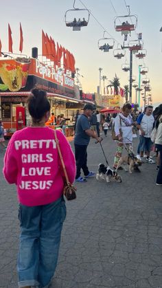 people are walking their dogs down the street in front of some shops and carnival rides