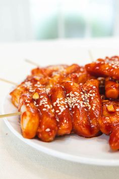 a white plate topped with chicken covered in sauce and sesame seeds on skewers