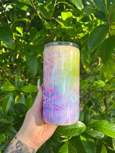 a hand holding up a colorful candle in front of green leaves