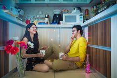 a man and woman sitting on the floor in a small kitchen eating cake, talking