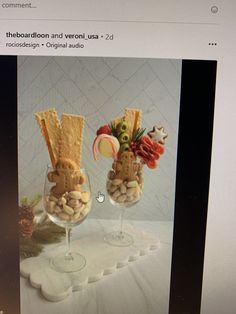 two wine glasses filled with snacks on top of a white tablecloth covered table next to a computer screen